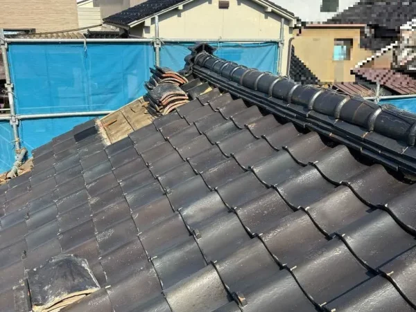 解体現場の屋根。瓦が順次めくられている写真。隣地との境には、養生シートが張られている。