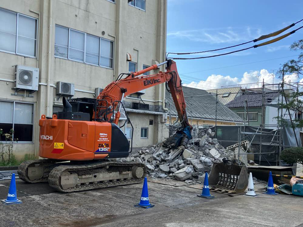 大割の油圧ショベルによって付属棟が解体され、瓦礫が積まれている。