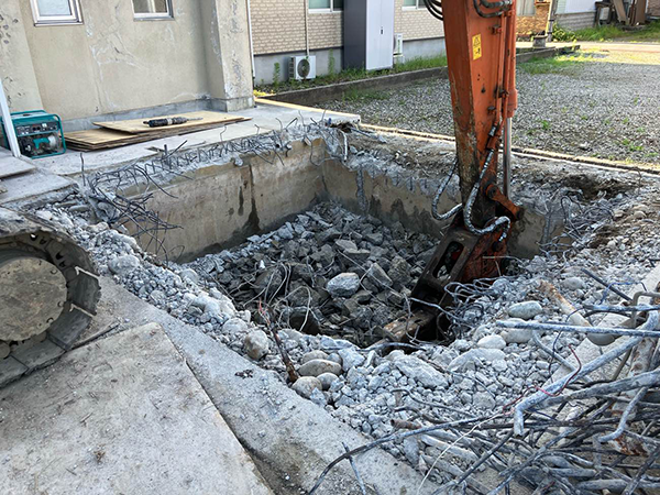 付属棟の床と基礎を、油圧ショベルのブレーカーで砕き、中心に四角形の穴が開いている。