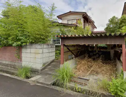 解体前の住宅と車庫の写真。塀と植栽も写っている。